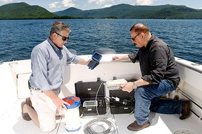    Weather stations  Weather stations in and around the lake will measure temperature, humidity, barometric pressure, wind velocity, rainfall, and the amount of sunlight present. Understanding the weather is very important, as it drives or affects many aspects of the Lake George ecosystem. They measure:      Wind Speed     Wind Direction     Temperature     Humidity     Pressure     Rainfall     Solar Irradiance    Vertical profilers  Vertical profilers are self-contained, floating, water-quality measurement stations. Mounted on a floating buoy are solar panels to collect energy, batteries to store the energy, a robotic winch to raise and lower sensors into the lake on a cable, computers to govern the entire system, GPS to monitor position, and communications equipment to transmit the data throughout the Jefferson Project cyber-infrastructure. The profilers are also equipped with weather stations.  They measure:      Conductivity     Temperature     pH     Dissolved Oxygen     Chlorophyll a (an index of phytoplankton)     Dissolved Organic Matter     Chloride    Tributary stations  Tributary stations measure many of the same water quality parameters as the vertical profilers as well as the flow and depth of the streams. Such data help researchers to understand the quality of the water flowing into Lake George. They measure:      Water flow and level     Conductivity     Temperature     pH     ORP (Oxidation-Reduction Potential)     Turbidity     Dissolved Organic Matter     Chloride     Dissolved Oxygen     Chlorophyll a (an index of phytoplankton)    Acoustic Doppler Current Profilers  Acoustic Doppler Current Profilers (ADCPs) are acoustic sensors that measure the direction and speed of currents within the lake in three dimensions.  They are currently deployed on the lake bottom and operate using the principles of SONAR technology, by the reflection of acoustic beams from suspended particles in the water. Ecosystem Monitoring  Surveying  Given the critical role that organisms in a food web play in determining water quality, the Jefferson Project has initiated an effort to comprehensively sample the food web of the lake, its associated wetlands, and the largest streams that supply the lake with water. In these habitats, we are surveying the plants, plankton, invertebrate animals, and major fish species to determine their abundance and distribution around the lake and throughout the year. These surveys include the monitoring of any invasive species that are present.  Lake Coring  Sediments skimmed and extracted from the lake bed using cores - hollow tubes pushed several feet into the mud - can offer valuable insight into historic environmental conditions. Researchers analyze samples to determine the presence and abundance of various microscopic plants and animals, as well as information on pollen, chemical isotopes, and metal contaminants. The surface sediment details present-day conditions, while the cores provide a biogeochemical history of the lake - with sediments in the deepest sections reaching back thousands of years.   Offshore Chemical Monitoring  For more than 35 years, DFWI has maintained the Offshore Chemical Monitoring Program. Begun in 1980 and jointly funded by RPI and The FUND for Lake George, the monitoring program was designed to assess water quality in order to help address concerns related to nutrient loading. Sampling focuses on essential nutrients for aquatic plants (phosphorus, nitrogen and silican compounds), as well as major cations, common anions, oxygen, chlorophyll, and temperature. Measurements are made at biweekly intervals during spring and fall, and at monthly intervals during summer, at a core set of six mid-water stations. Samples are collected using a depth-integrated sampler from the surface to 10-meter depth with grab samples taken at 20-30 meter depths, typically within 1-meter off the lake bottom to characterize the hypolimnetic water. Temperature and oxygen are measured at discrete depths extending to 30-meters to characterize the density structure of the water column and its oxygen concentration. Configure Deploying a vertical profiler.    IBM Research scientists examine sensor technology used in the Jefferson Project.